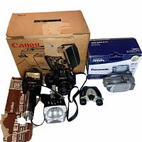 Overview of all items with their original boxes and arrangement showing the Canon Cine Projector, Kako Auto-Elite external flash strobe, LPL flood/spot light, Panasonic video camera, and binoculars.