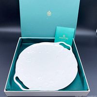 White fine china serving plate embossed with strawberry motifs shown seated inside a teal box with a matching booklet, photo taken to show included packaging and brand.