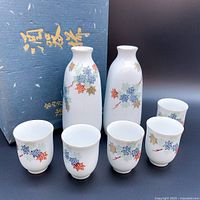 Overall view of the Fukagawa Seiji porcelain sake set with two carafes and five cups, showing floral pattern decoration and original box.