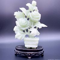 Front view of carved green stone rose sculpture with wooden base, showing multiple flowers and leaves.