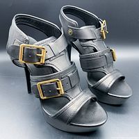 Pair of black Italian leather strappy high heel sandals shown from front-left angle, highlighting gold-tone buckles and open toe design.