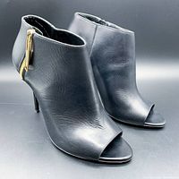 Front angle view of the pair of black Italian leather peep-toe high heel sandals with gold zipper on back and stiletto heel.