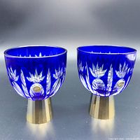 Front view of pair of cobalt blue glass sake cups showing cut glass pattern and gold bases