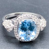 Close-up image of the ring showing the oval blue topaz main stone set in silver with small white topaz stones around the halo and sides.