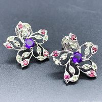 Front view of the stud earrings showing flower shape with round purple amethyst centers and green peridot and red rhodolite stones.