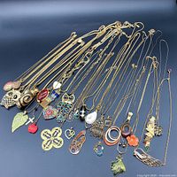 Full view of 21 gold-tone pendant necklaces laid out on black surface showing variety of pendant styles and chains.