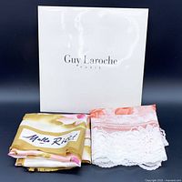 Detailed view of folded Melle Ricci floral silk scarf beside folded Guy Laroche silk scarf with lace detailing and their branded packaging.