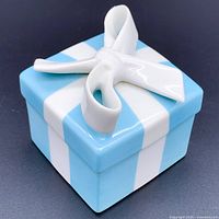 Square porcelain trinket box painted Tiffany blue with vertical white stripes and topped with a white porcelain bow.