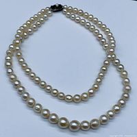 Full view of two pearl strands laid flat showing graduated sizing and clasp position
