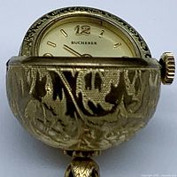 Close-up of the watch face partially opened showing brand name and textured gold-plated case.