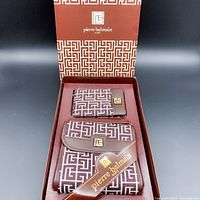 Photo of the set in original branded box showing cosmetic pouch and mirror case with Pierre Balmain logo print and brown leather trim.