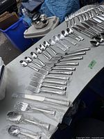 Wide view of forks and spoons arranged on table, several wrapped in plastic