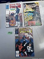 Photo showing three Spider-Man comic books on a white surface. One Marvel Tales Spider-Man featuring Punisher and two Amazing Spider-Man editions. Covers show visible signs of wear including creases, discoloration, and edge wear.