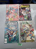 Photo showing 4 Avengers comic books laid flat with visible cover art, including Captain America, Scarlet Witch, and other Avengers characters.