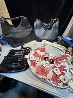 Photo showing all four purses in the lot on a surface, two Michael Kors black leather purses and two Guess purses including floral print and glossy black.