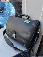 Front view of the black leather Samsonite briefcase placed on a surface showing flap closure and shoulder strap.