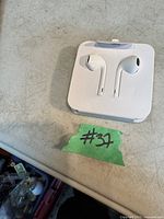 Photo of new Apple EarPods in original packaging showing white wired earbuds in plastic holder on a table.