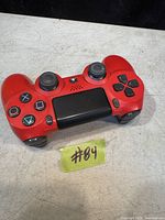 Red PlayStation 4 DualShock 4 wireless controller with standard button layout and touchpad, shown on flat surface with lot number displayed.