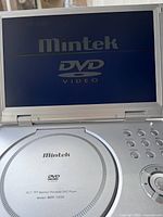 Open Mintek portable DVD player showing screen and controls with Mintek DVD logo on screen.