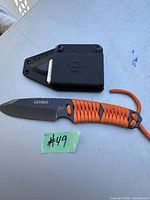 Photo showing the Gerber fixed blade knife with an orange wrapped handle and the black plastic sheath beside it.