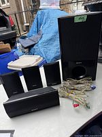 Photo showing 4 satellite speakers and 1 subwoofer speaker with wired connections laid out on a table.