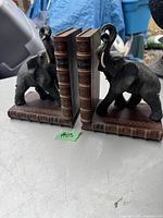Pair of vintage black elephant bookends with book-shaped bases shown holding books between them.
