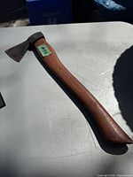 Full view of the vintage small axe lying flat on a table showing the entire wooden handle and metal axe head with visible use and age.