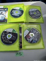 Four Xbox 360 game discs visible in lime green cases, titles Portal 2, Ace Combat 6, Hunted, and The Club
