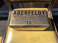 Top exterior of rectangular metal tin showing Aberfeldy Highland Single Malt Scotch Whisky raised lettering and 12 year age statement.