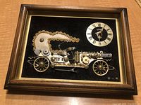 Framed antique car art composed of small metal hardware pieces with a clock, displayed in a wood frame.