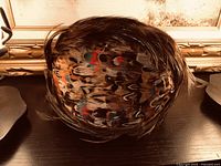 Top view of an antique feather cap showing multicolored feathers with details in brown, beige, red, and black.