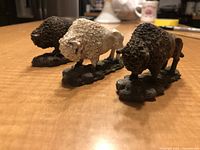 Front angle of three buffalo figurines showing two brown and one white with bases, placed on a table surface.