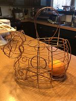 Metal wire basket in the shape of a cow holding an orange, placed on kitchen counter.