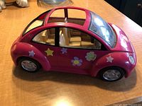 Side view of pink Fisher Price Volkswagen toy car showing stickers of stars and flowers and beige seats inside.