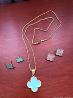 Photo showing full view of gold plated 16-inch chain necklace with light blue enamel clover pendant and two pairs of clover-shaped earrings in green enamel and mother of pearl.