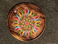 Full view of the round wood turned plate showing the colorful geometric starburst pattern painted on the surface.