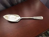 Server spoon laid flat on wooden surface showing full length and handle.