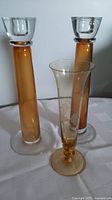 Photo showing two amber glass candleholders and one clear etched glass vase on a white tablecloth.
