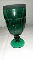 Green depression glass goblet with faceted bowl and stem photographed on a white surface.