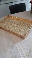 View of the finished rectangular wood tray with gold veneer in mosaic pattern resting on a table with a fabric runner underneath. Shows front and top surfaces.