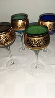 Four colored glass wine glasses with twisted stems and gold embossed floral patterns