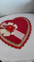 Full view of red heart-shaped gift box with ruffled trim and floral bow decoration