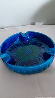 Front angled view of large blue ceramic ashtray showing flower design and 3 cigarette rests