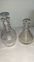Pair of vintage crystal decanters on a white cloth against gray background, showing different shapes and sizes.