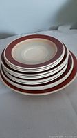 Stack of various plate sizes showing the concentric ring red and cream band design on Susie Cooper Wedding Band dishware.