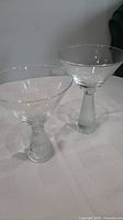 Two clear Scandinavian style martini glasses, one with a flared textured heavy base and the other with a slim smooth base.