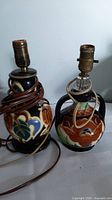 Two vintage Gouda pottery lamps with floral and abstract patterns, showing cord wrapped around one lamp base and aged bulb sockets.