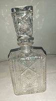 Front and top view of vintage crystal decanter showing intricate cut glass geometric designs and fitted stopper.