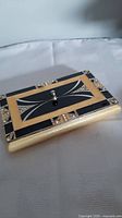 Closed rectangular metal jewellery box with black and gold geometric design embellished with stones and a central knob on lid.