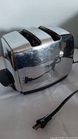 Angled view of the vintage two-slot chrome toaster showing reflective metal surface, plug, and side control knob.